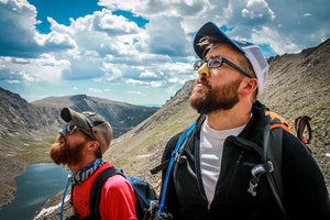 Two hikers wearing colorful, environmentally-safe Nöz sunscreen while adventuring in the mountains